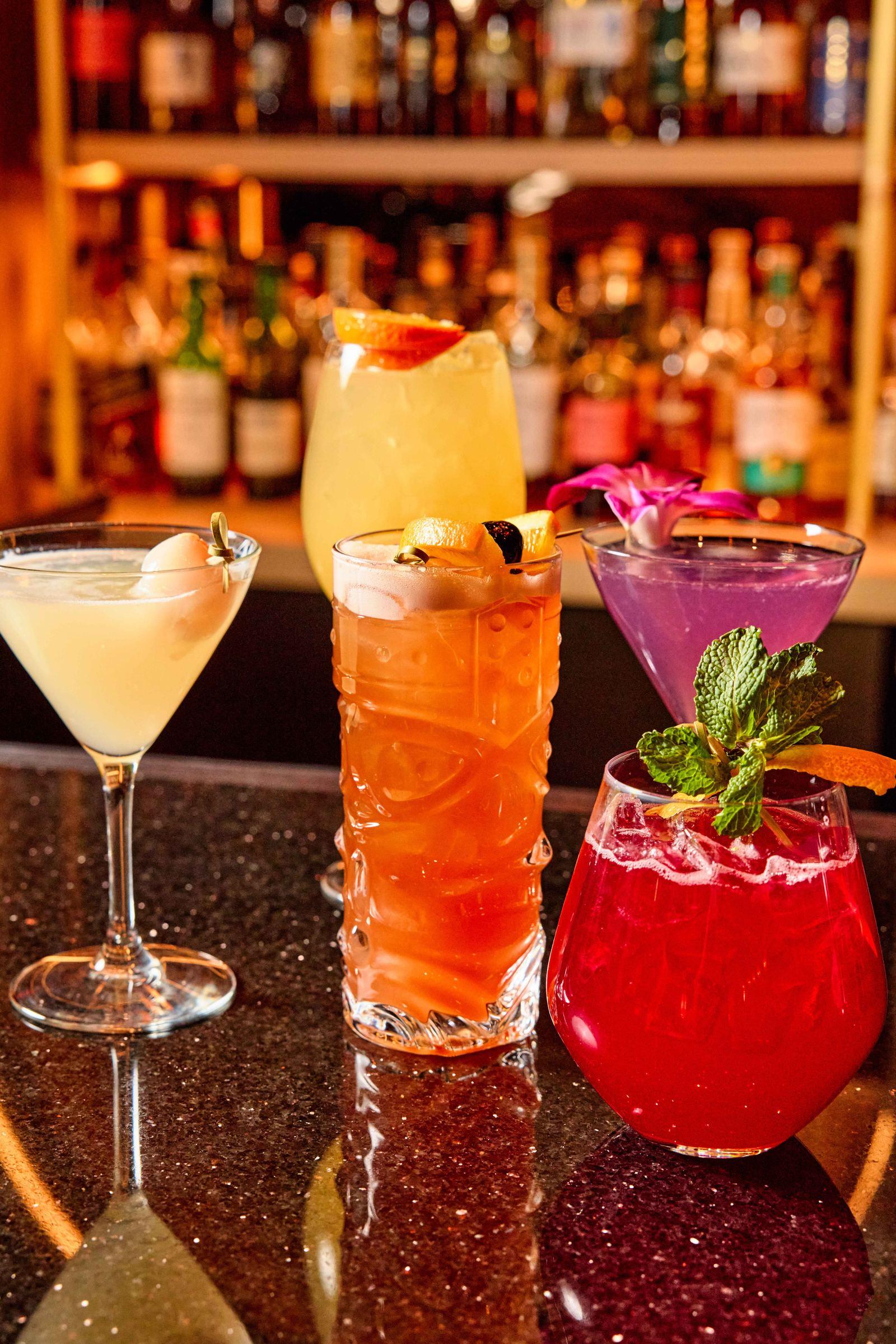 A lineup of Douzo's colorful signature cocktails on the bar, with the back bar's bottles in the background